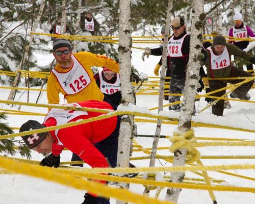 Participants navigate a snowy course, weaving through trees and yellow ropes during a winter race.