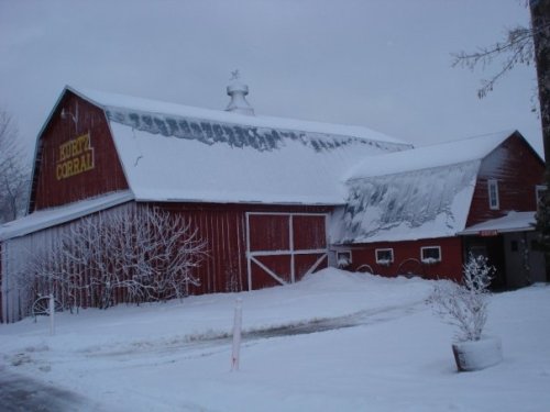 A red barn with a snowy roof and surrounding snow-covered ground, set against a gray winter sky.