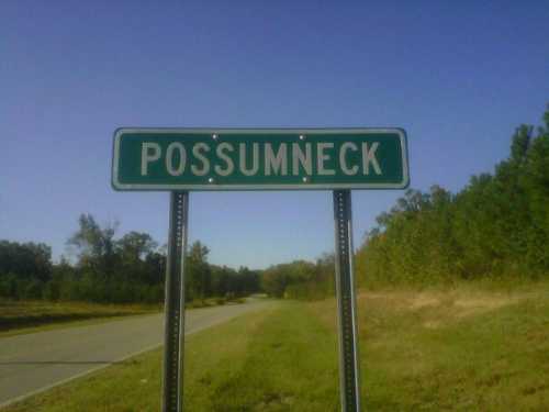 Sign for Possumneck on a rural road, surrounded by trees and clear blue sky.