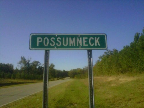 Sign for Possumneck on a rural road, surrounded by trees and clear blue sky.