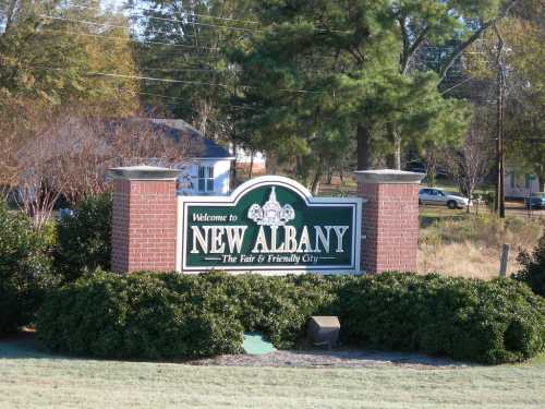 Welcome sign for New Albany, featuring the tagline "The Fair and Friendly City," surrounded by greenery.