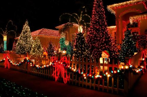 A festive display of colorful Christmas lights, decorated trees, and holiday decorations in a yard.
