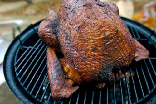 A smoked turkey resting on a grill, showcasing a dark, crispy skin and juicy appearance.