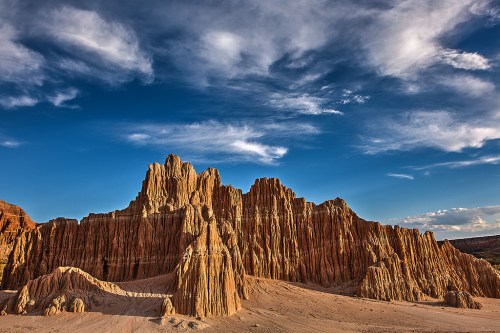 A dramatic landscape of rugged, orange rock formations under a blue sky with scattered clouds.