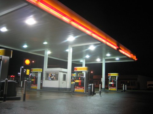 A brightly lit gas station at night, featuring multiple fuel pumps and a convenience store.