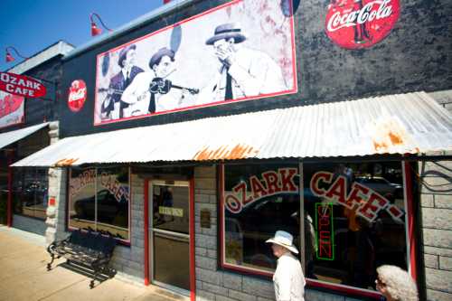 A rustic cafe with a corrugated metal roof, featuring vintage Coca-Cola signs and black-and-white photos on the wall.