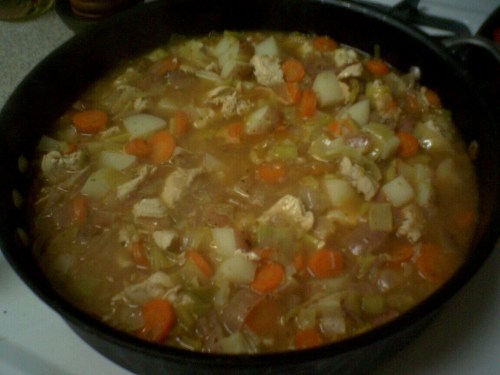 A pot of chicken soup filled with carrots, potatoes, celery, and noodles simmering on the stove.