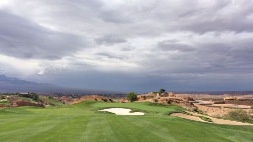 A scenic golf course with lush green grass, a sand trap, and a dramatic cloudy sky in the background.