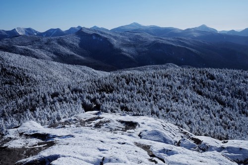 A panoramic view of snow-covered mountains and forests under a clear blue sky.