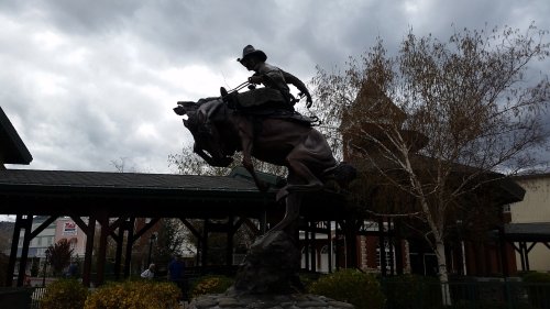 A bronze statue of a cowboy riding a bucking horse, set against a cloudy sky.