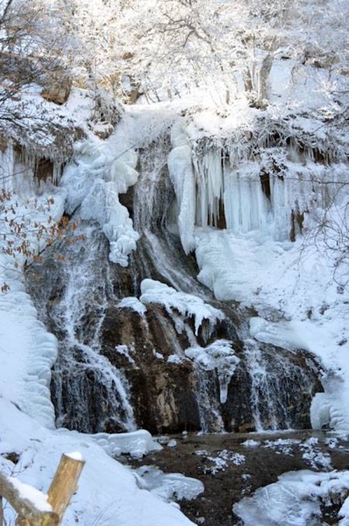 A frozen waterfall surrounded by snow-covered rocks and icicles, creating a serene winter landscape.