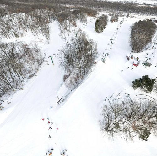 Aerial view of a snowy ski resort with ski lifts and trails surrounded by trees.