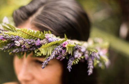 A close-up of a woman wearing a floral crown made of purple and green flowers and leaves.