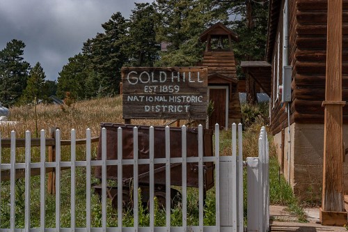 Sign for Gold Hill National Historic District, established in 1859, with a wooden structure and a white picket fence.