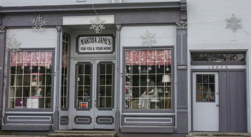 A charming storefront with large windows, displaying home goods and festive decorations, labeled "Martha Jane's."