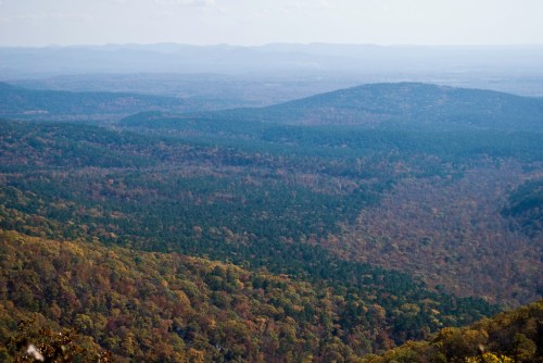 A panoramic view of rolling hills and valleys covered in autumn foliage under a clear sky.