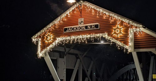A covered bridge in Jackson, NH, adorned with festive lights, illuminated at night.