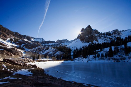 A serene winter landscape featuring a frozen lake, snow-covered mountains, and a clear blue sky.