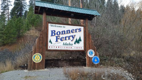 Welcome sign for Bonners Ferry, Idaho, established in 1899, with logos of local organizations and a forested background.