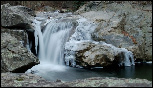 A serene waterfall cascades over rocks, surrounded by a tranquil forest setting.