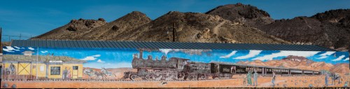 A colorful mural depicting a steam train, station, and figures against a mountainous backdrop.