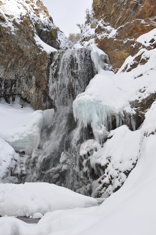 A frozen waterfall surrounded by snow-covered rocks and icicles, creating a serene winter landscape.