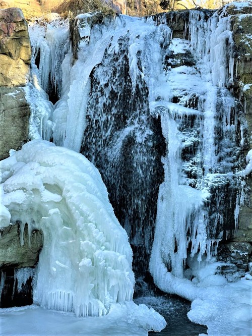 A frozen waterfall with icicles and snow-covered rocks, creating a serene winter landscape.