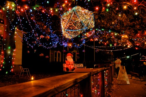 Colorful holiday lights adorn trees and decorations, creating a festive atmosphere at night. A Santa figure is visible.