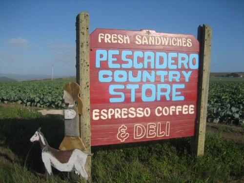 Sign for Pescadero Country Store featuring fresh sandwiches, espresso coffee, and deli, with a wooden figure and goat.
