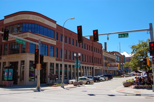 A sunny street view of a downtown area with shops, traffic lights, and outdoor seating at cafes.