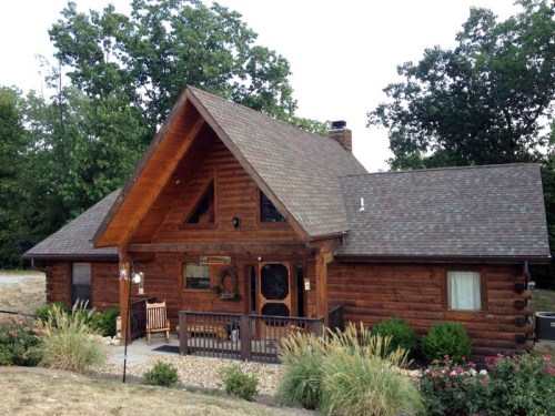 A charming log cabin with a steep roof, surrounded by greenery and a small garden in front.