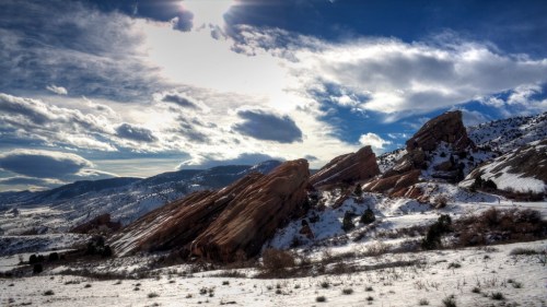 Snow-covered landscape with red rock formations under a cloudy sky, showcasing a serene winter scene.