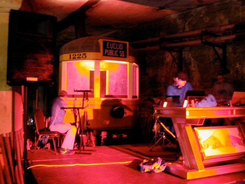 A dimly lit room featuring a vintage tram and two people working at a table, with colorful lighting effects.