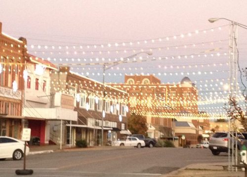 A charming street lined with buildings, adorned with string lights glowing in the evening sky.