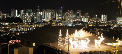 A rooftop decorated with holiday lights, overlooking a city skyline at night.
