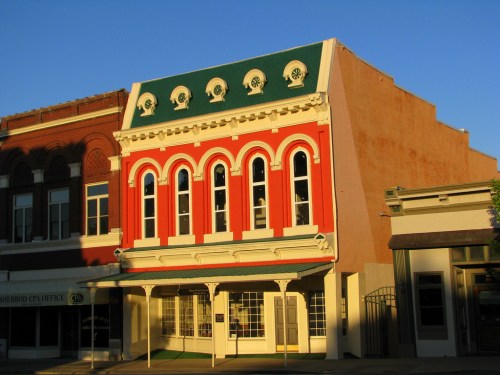 Historic building with a colorful facade, featuring arched windows and a green roof, bathed in warm evening light.