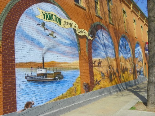 Colorful mural depicting Yankton, South Dakota, featuring a riverboat, wildlife, and historical scenes on a brick wall.