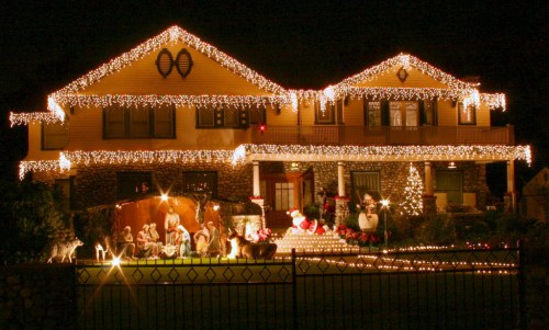 A beautifully decorated house at night, adorned with festive lights and holiday decorations, including Santa and reindeer.