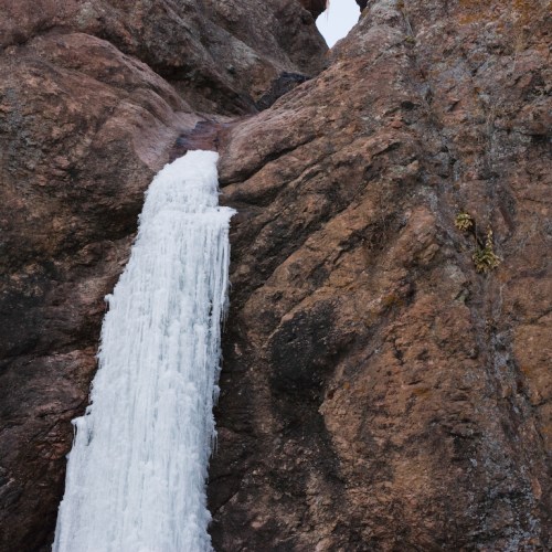 A cascading waterfall flows down a rocky cliff, surrounded by rugged terrain and natural textures.