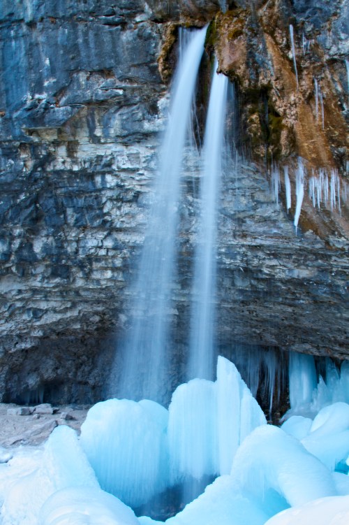 A frozen waterfall cascading over icy rocks, surrounded by blue ice formations and icicles.