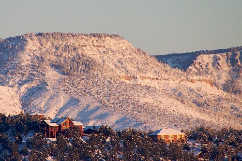 Snow-covered mountains with a few houses in the foreground, bathed in soft morning light.