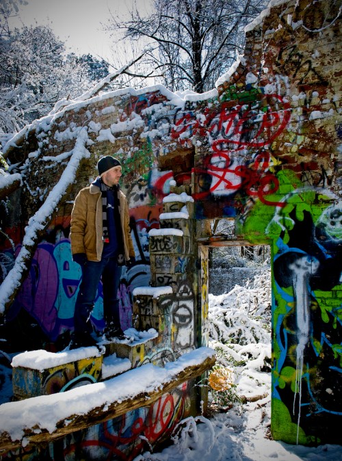 A person stands on a snowy, graffiti-covered ruin, surrounded by vibrant colors and winter scenery.