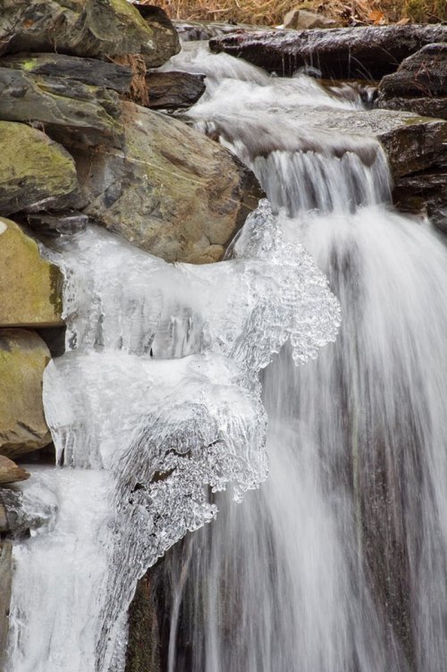 A close-up of a waterfall cascading over rocks, with ice formations along the edges.