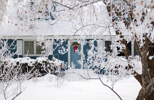 A blue house with a decorated door surrounded by snow-covered trees and a winter landscape.