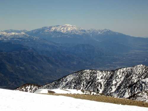 Snow-capped mountains under a clear blue sky, with valleys and ridges visible in the foreground and background.