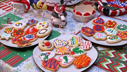 Colorful decorated cookies on plates, surrounded by festive holiday-themed tableware and a cheerful tablecloth.