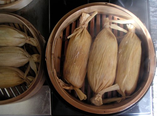 Steamed tamales wrapped in corn husks, arranged in a bamboo steamer.