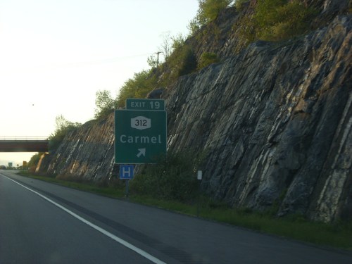 Highway exit sign for Carmel, Exit 19, with rocky terrain in the background.