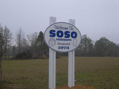 Welcome sign for Soso, Mississippi, with the year of incorporation, 1973, surrounded by trees and a cloudy sky.