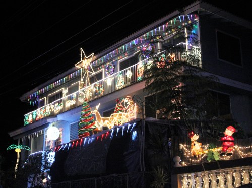 A house decorated with colorful Christmas lights, featuring a star, tree, and festive figures, all illuminated at night.